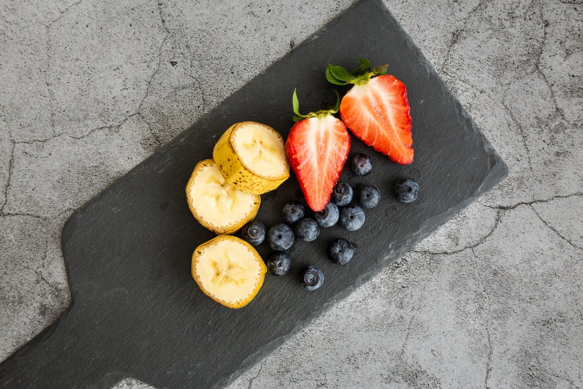 Tabla negra de cocina con plátano, uvas y fresas para pasabocas sencillos