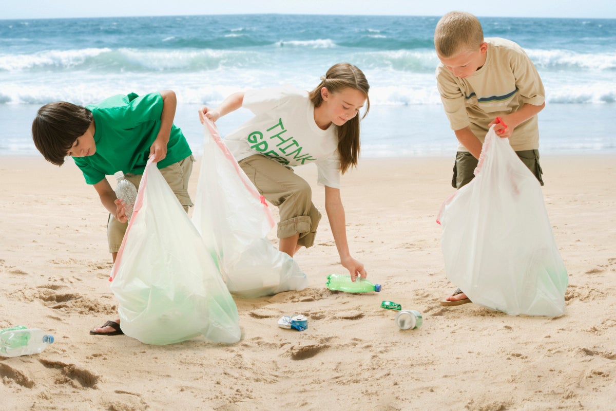 Dos niños y una niña recogiendo botellas plásticas de una playa contaminada