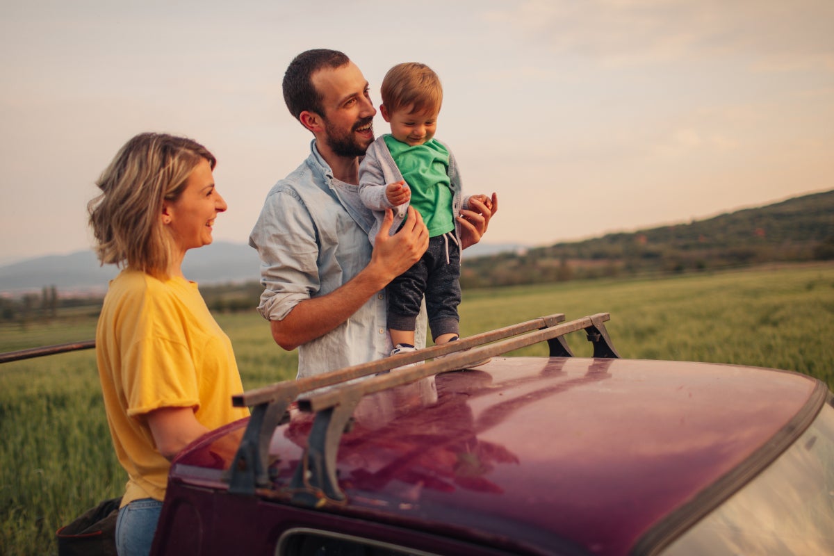 Mujer, hombre y niño viendo el paisaje del viaje al lado del carro.