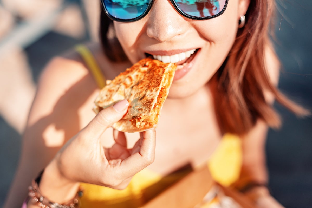 Mujer comiendo en un picnic en la playa con gafas oscuras