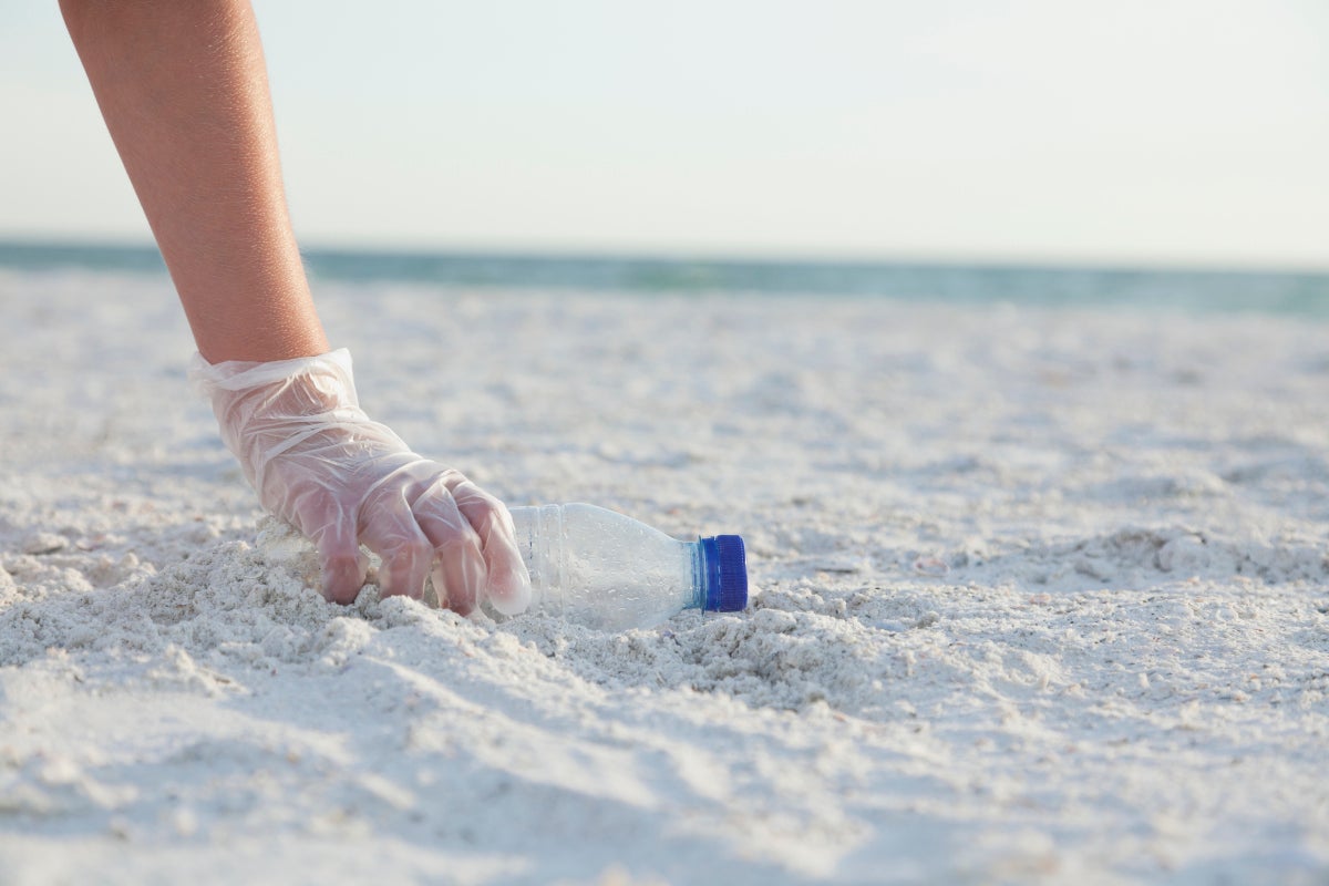 Mano recogiendo una botella en la playa luego de hacer un picnic