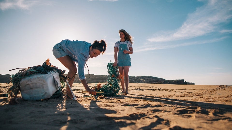 Dos mujeres en la playa recogiendo basura en la arena.