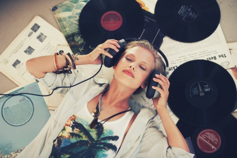 Mujer acostada encima de unos discos con sus audífonos escuchando música